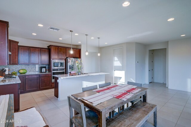 kitchen with an island with sink, light stone countertops, stainless steel appliances, and decorative light fixtures