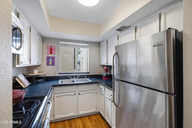 kitchen featuring stainless steel appliances, a sink, dark countertops, white cabinetry, and light wood finished floors