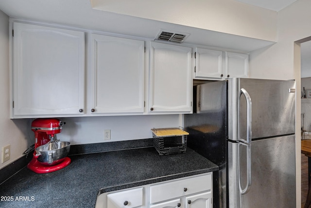kitchen with dark countertops, freestanding refrigerator, and white cabinetry