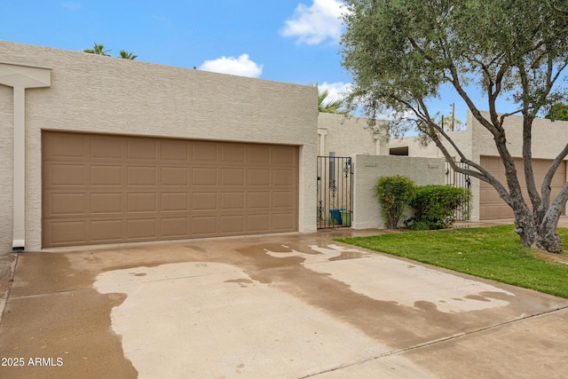 pueblo-style home featuring stucco siding, a garage, a gate, and concrete driveway