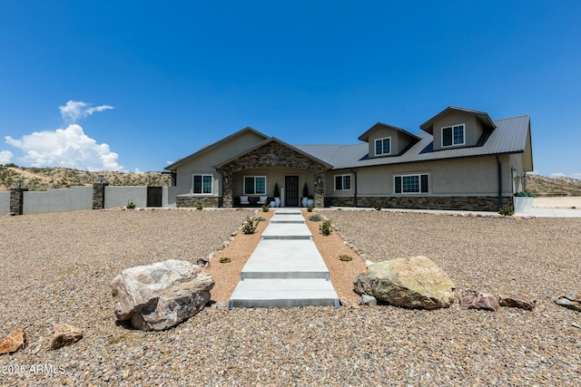 view of front of home with stone siding, fence, metal roof, and stucco siding