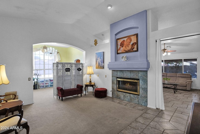 carpeted living room featuring ceiling fan with notable chandelier, a tiled fireplace, and vaulted ceiling