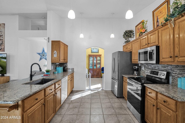 kitchen featuring appliances with stainless steel finishes, sink, light tile patterned floors, decorative light fixtures, and a high ceiling