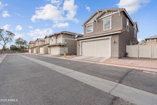 view of front of property featuring a garage, concrete driveway, a residential view, fence, and stucco siding