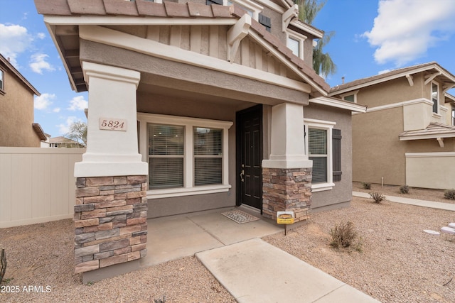 doorway to property featuring stone siding, fence, and stucco siding