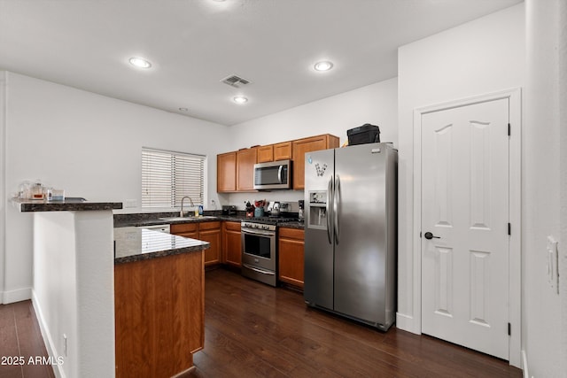 kitchen featuring stainless steel appliances, dark wood-style flooring, brown cabinets, and a peninsula