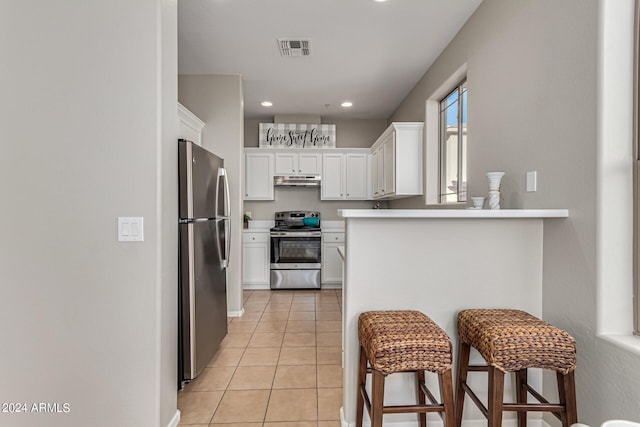 kitchen with kitchen peninsula, white cabinets, a kitchen bar, light tile patterned flooring, and stainless steel appliances