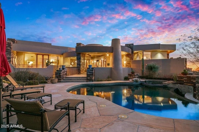 pool at dusk featuring an in ground hot tub and a patio