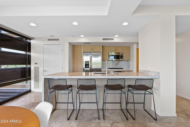 kitchen featuring sink, backsplash, kitchen peninsula, a kitchen bar, and appliances with stainless steel finishes