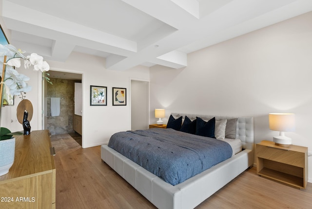 bedroom featuring beam ceiling, light wood-type flooring, ensuite bathroom, and coffered ceiling