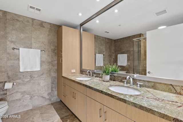 bathroom with vanity, toilet, a shower with door, and tile walls