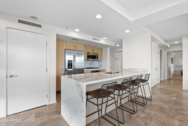 kitchen featuring kitchen peninsula, appliances with stainless steel finishes, tasteful backsplash, sink, and light brown cabinets