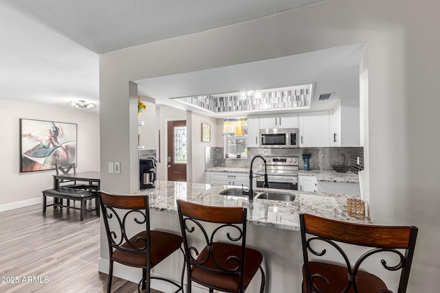 kitchen with white cabinets, appliances with stainless steel finishes, a sink, backsplash, and visible vents