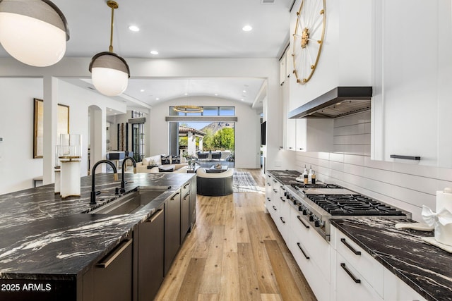 kitchen featuring stainless steel gas cooktop, a sink, open floor plan, wall chimney range hood, and light wood finished floors