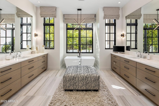 full bathroom with baseboards, two vanities, a sink, and a freestanding bath