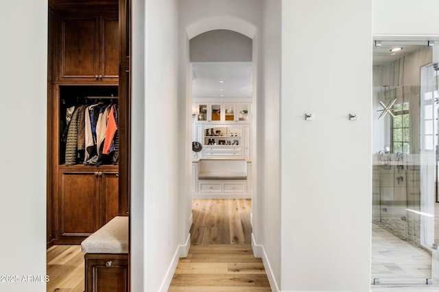 corridor with light wood finished floors, baseboards, and arched walkways