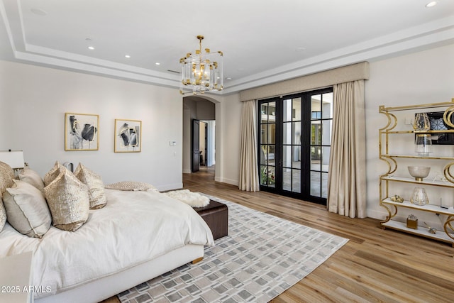 bedroom featuring arched walkways, recessed lighting, a raised ceiling, wood finished floors, and baseboards