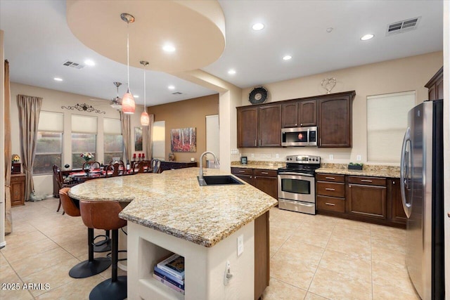 kitchen with stainless steel appliances, a center island with sink, decorative light fixtures, and sink