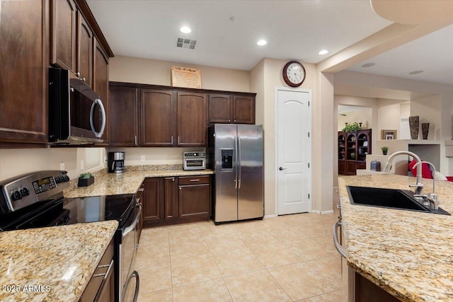 kitchen featuring light stone counters, appliances with stainless steel finishes, dark brown cabinetry, and sink