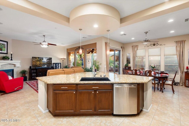 kitchen with a kitchen island with sink, pendant lighting, light stone counters, sink, and stainless steel dishwasher