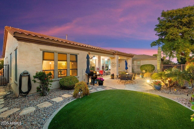 back house at dusk featuring a patio and a lawn