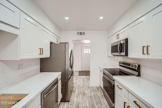 kitchen featuring appliances with stainless steel finishes, wood tiled floor, light stone counters, and white cabinets