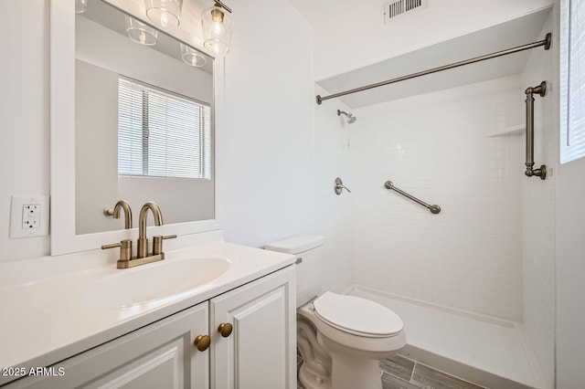 full bath featuring visible vents, tiled shower, toilet, wood finished floors, and vanity