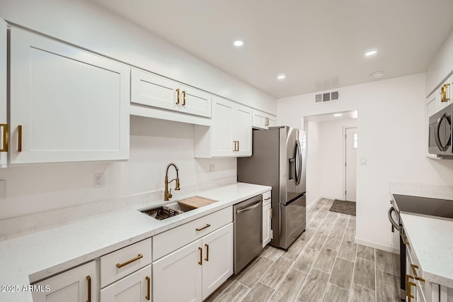 kitchen featuring light stone counters, visible vents, appliances with stainless steel finishes, white cabinets, and a sink