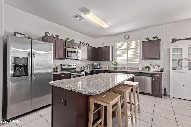 4741 E Fire Opal Ln, San Tan Valley, AZ 85143 - kitchen featuring stainless steel appliances, light tile patterned floors, dark brown cabinetry, a sink, and a kitchen bar