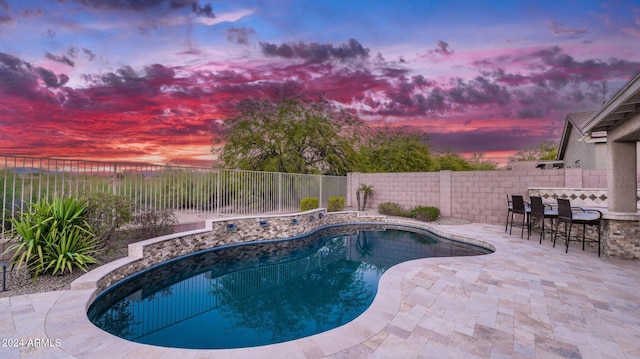 pool at dusk with exterior bar and a patio