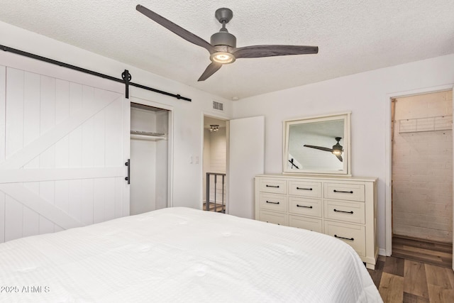 8538 E Portland St, Scottsdale, AZ 85257 - bedroom featuring wood finished floors, a barn door, a closet, a textured ceiling, and a ceiling fan
