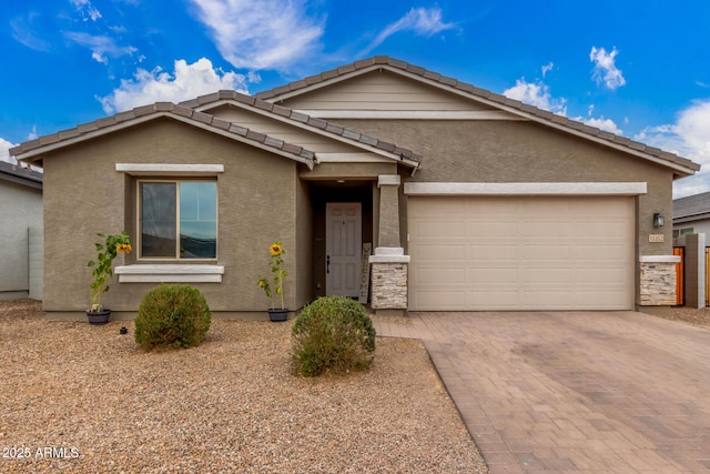 ranch-style home featuring decorative driveway, stucco siding, an attached garage, stone siding, and a tiled roof