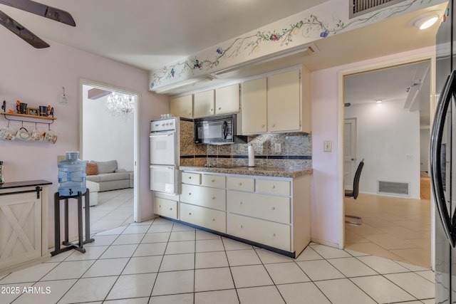 kitchen with light tile patterned floors, tasteful backsplash, black appliances, stone countertops, and cream cabinetry