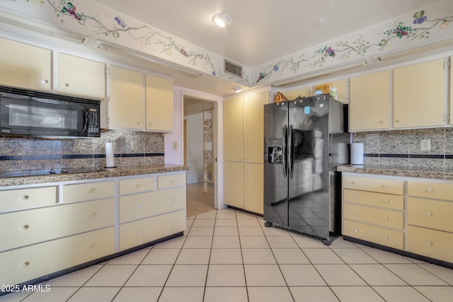 kitchen featuring light tile patterned floors, stone counters, backsplash, black appliances, and cream cabinetry