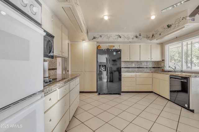 kitchen featuring sink, black appliances, light tile patterned floors, cream cabinetry, and backsplash