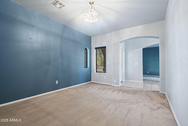 spare room featuring light carpet and a notable chandelier