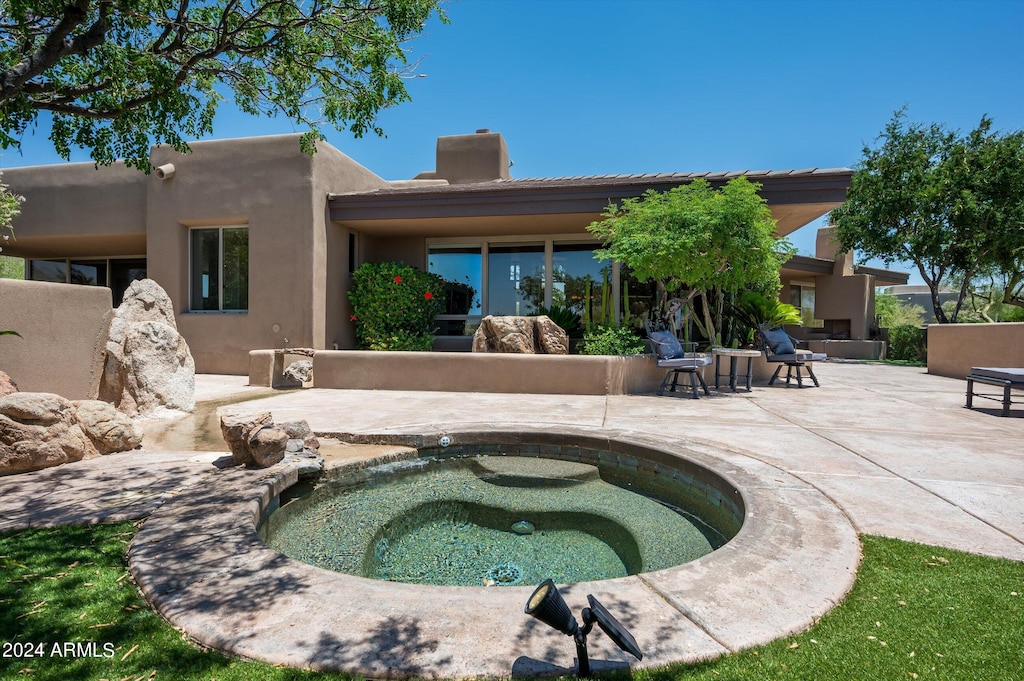 rear view of house featuring an in ground hot tub and a patio area