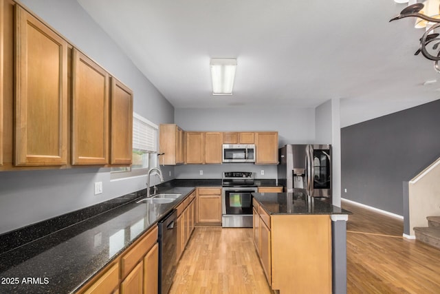 kitchen featuring a sink, a kitchen island, light wood finished floors, stainless steel appliances, and dark stone counters
