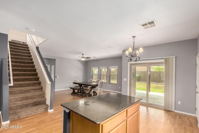 kitchen with light wood-type flooring, a kitchen island, ceiling fan with notable chandelier, and visible vents