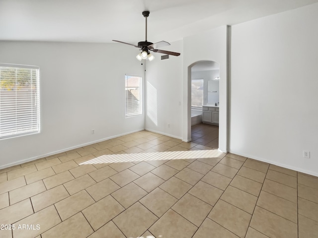 empty room featuring vaulted ceiling, a healthy amount of sunlight, light tile patterned floors, and ceiling fan