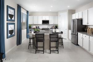 kitchen featuring a kitchen bar, white cabinets, recessed lighting, freestanding refrigerator, and a center island with sink