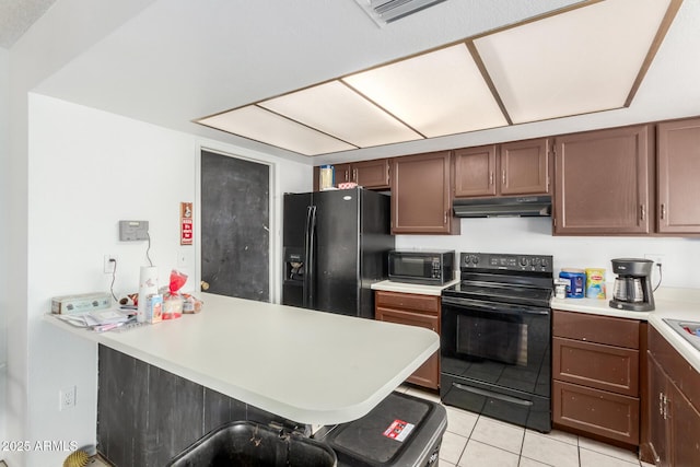 kitchen featuring light tile patterned floors, kitchen peninsula, a kitchen bar, and black appliances