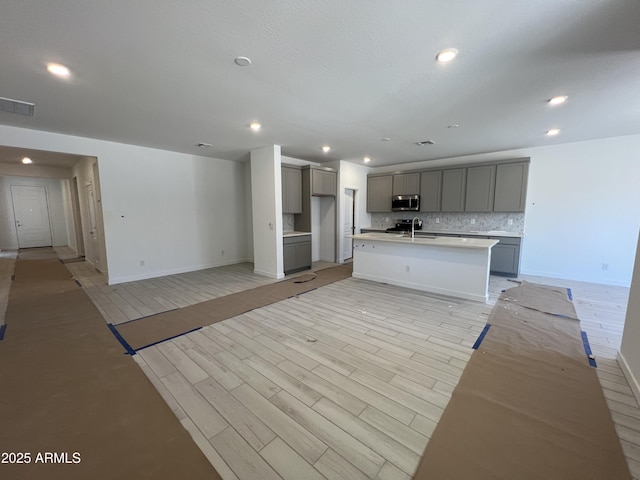 kitchen featuring a sink, light wood-type flooring, backsplash, gray cabinets, and stainless steel microwave