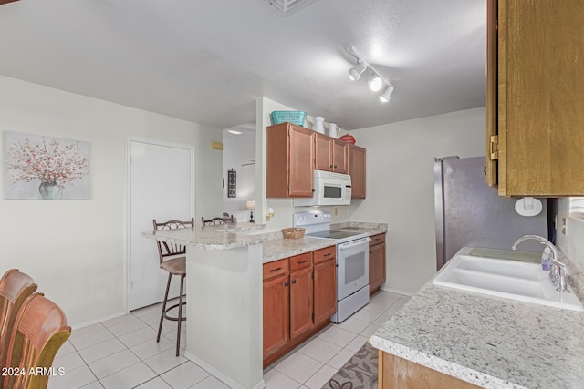 kitchen featuring kitchen peninsula, white appliances, sink, light tile patterned floors, and a breakfast bar area