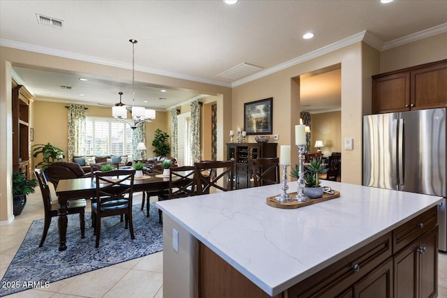 kitchen with visible vents, ornamental molding, open floor plan, light stone counters, and freestanding refrigerator