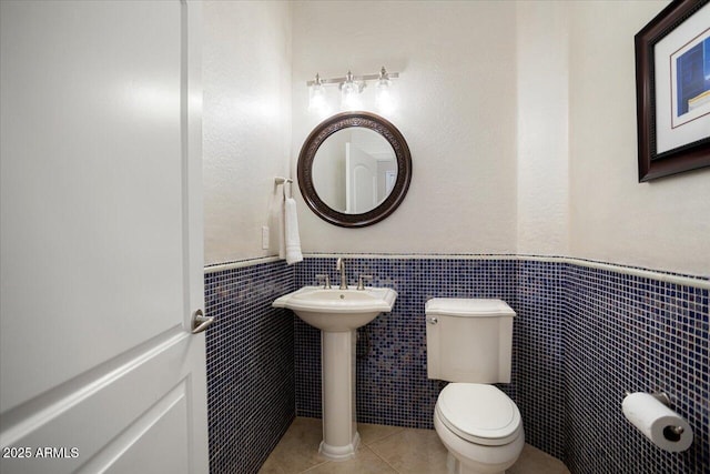 half bathroom featuring toilet, a wainscoted wall, tile walls, and tile patterned floors