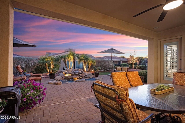 patio terrace at dusk with outdoor dining area and a ceiling fan