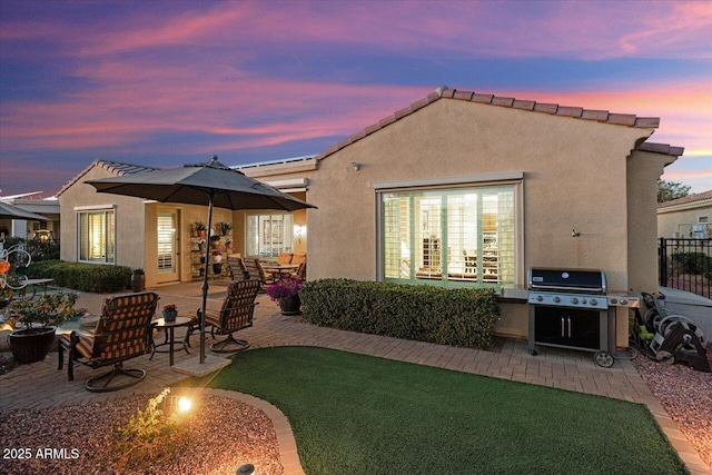 back of property at dusk featuring a patio, a yard, and stucco siding