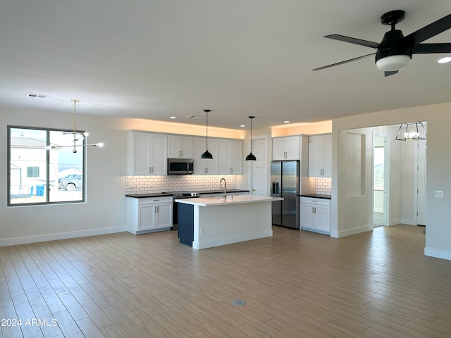 kitchen with a wealth of natural light, appliances with stainless steel finishes, hanging light fixtures, and white cabinets