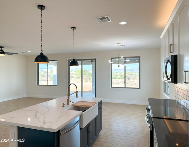 kitchen with stainless steel appliances, a wealth of natural light, decorative light fixtures, and an island with sink